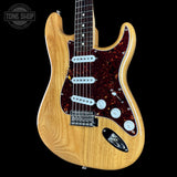 A classic electric guitar with a natural wood finish body, a dark red and black tortoiseshell pickguard, and white hardware, shown against a solid black background.