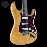 A classic electric guitar with a natural wood finish body, a dark red and black speckled tortoiseshell pickguard, and chrome hardware, shown against a solid black background with a Tone Shop watermark in the top left corner.