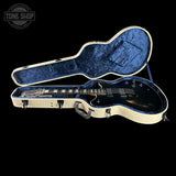 Guitar in an open case with a black background and 'Tone Shop' logo.