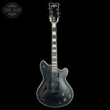 Electric guitar with a silver finish on a black background, featuring the 'Tone Shop' logo.
