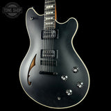 Black electric guitar with decorative elements on a black background, featuring the Tone Shop logo.