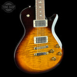 A close-up of a Gibson electric guitar body featuring a vibrant sunburst finish that transitions from a bright amber-orange center to a dark brown edge. The guitar has chrome hardware, gold-toned control knobs, and a dark fretboard with white inlays, set against a solid black background.