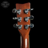 Close-up of the headstock of an acoustic guitar, showing six tuning pegs and a glossy reddish-brown wood finish against a black background. A Tone Shop watermark is visible in the top-left corner.
