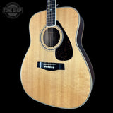 A natural wood acoustic guitar shown from a front three-quarter angle against a solid black background, with a Tone Shop watermark in the upper left corner.