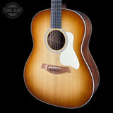 A Taylor acoustic guitar with a natural sunburst finish, dark wood sides, and a white pickguard, shown against a solid black background with a Tone Shop watermark in the top-left corner.
