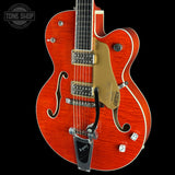 A close-up studio shot of a red-orange electric guitar against a black background, showing the body, f-holes, gold-toned pickguard, chrome hardware, and part of the neck. A Tone Shop watermark appears in the top-left corner.