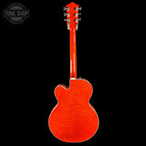 The back view of an electric guitar with a vibrant orange-red cherry wood finish, shown against a solid black background with a Tone Shop watermark in the top left corner.