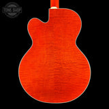 Close-up of the back of an electric guitar body with a vibrant orange-red flamed maple wood finish and white binding, shown against a solid black background with a Tone Shop watermark in the top left.