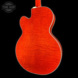 The back of an acoustic guitar with a vibrant orange-red flamed maple top, white binding, and a matching neck, shown against a solid black background with a Tone Shop watermark in the top left corner.