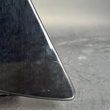 Close-up of a glossy black guitar body corner with visible scratches and a gray concrete floor in the background.