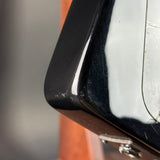 Close-up detail of a glossy black guitar body corner with a silver control plate and visible wear or scuffs on the surface.