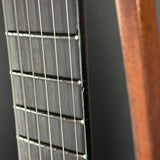 Close-up detail of an acoustic guitar's dark fretboard with six strings and a warm brown wooden body edge, set against a dark background.