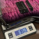 A close-up of an electric guitar body resting on a digital scale, showing a purple/magenta flamed maple wood finish and black hardware. The scale displays a weight of 8.