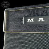 Close-up of a black textured amplifier cabinet with a black front plate, white lettering, and gold trim on a black background. A Tone Shop watermark is visible in the top-left corner.