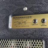 Close-up of a Magnatone Super Fifty-Nine amplifier head showing the gold metal plate with the brand name, signature, and input jacks on a dark textured grille.