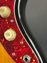 Close-up of a guitar with red flame pattern and gold knobs on a black background