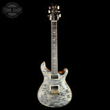 A custom electric guitar with a distressed silver and black flamed maple body, set against a solid black background. The headstock is dark wood with gold hardware, and a Tone Shop watermark is visible in the top left corner.