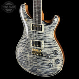 A close-up of an electric guitar body with a silver and black flamed maple wood finish, featuring gold hardware and a dark fretboard, set against a solid black background.