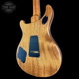 The back of an electric guitar with a natural wood finish and dark blue pickguard covers, shown against a solid black background with a Tone Shop watermark in the top left corner.