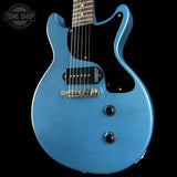 Blue electric guitar with a black pickguard on a black background, featuring the Tone Shop logo.