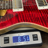 A close-up of a red electric guitar body resting on a digital scale showing a weight of 8 lbs 5 oz.