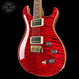 A red electric guitar with a vibrant flamed maple wood finish, gold hardware, and a gold neck, shown against a solid black background with a Tone Shop watermark in the top left corner.
