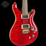 A red electric guitar with a flamed maple wood finish, gold hardware, and a dark fretboard, shown against a solid black background with a Tone Shop watermark in the top left corner.