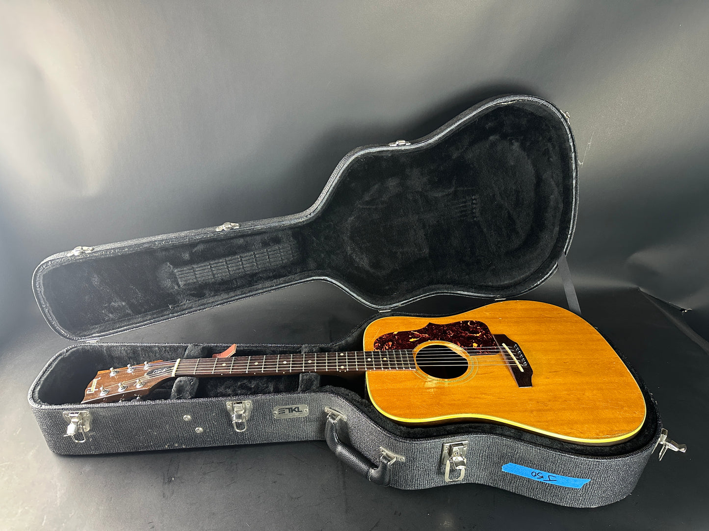Acoustic guitar in an open hard-shell case on a gray background