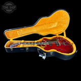 Red electric guitar in an open black and yellow case with 'Tone Shop' branding.