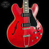 Red electric guitar with a black pickguard on a black background, featuring the Tone Shop logo.