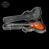 An electric guitar with a flame maple body in a sunburst orange finish, displayed inside an open black hard case on a solid black background. A Tone Shop watermark is visible in the top-left corner.
