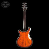 A classic six-string electric guitar shown from the back, featuring a vibrant orange-to-brown sunburst flamed maple top and a dark wood neck, set against a solid black background with a Tone Shop watermark in the upper left.
