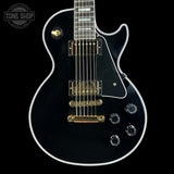 Black electric guitar with gold hardware on a black background, featuring 'Tone Shop' branding.