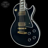 Black electric guitar with gold hardware on a black background, featuring 'Tone Shop' logo.