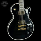 Black electric guitar with gold hardware on a black background, featuring 'Tone Shop' logo.