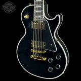 Black electric guitar with gold hardware on a black background, featuring 'Tone Shop' logo.