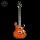A classic electric guitar with a vibrant orange-to-brown sunburst flame finish, shown against a solid black background. The headstock features the Paul Reed Smith (PRS) logo, and the neck has silver maple inlays.