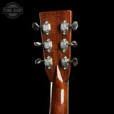 Close-up of the headstock of an acoustic guitar with six silver tuning pegs and a glossy reddish-brown wood finish, set against a solid black background. A 'TONE SHOP' watermark is visible in the top left corner.