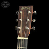 Close-up of the headstock of a Martin & Co acoustic guitar against a solid black background, showing the dark wood grain, gold script logo, and silver tuning pegs.