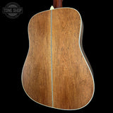 The back of an acoustic guitar with a rich brown wood finish and a white binding edge, shown against a solid black background with a Tone Shop watermark in the top left.
