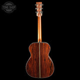 The back of an acoustic guitar with a rich reddish-brown wood finish and a gold-toned center stripe, shown against a solid black background with a Tone Shop watermark in the top-left corner.
