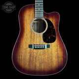A front-facing acoustic guitar with a natural wood sunburst finish, black pickguard, and black bridge, shown against a solid black background with a Tone Shop watermark in the top-left corner.