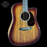 A close-up of a wooden acoustic guitar body with a natural brown to dark brown sunburst finish, featuring a cutaway body, sound hole, pickguard, and bridge, shown against a black background with a Tone Shop watermark in the top left.