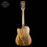 The back view of a wooden acoustic guitar with a rich natural wood grain finish, shown against a solid black background with a Tone Shop watermark in the top left corner.