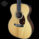 An acoustic guitar with a natural wood top, dark brown sides, and a tortoiseshell pickguard, shown against a solid black background with a Tone Shop watermark in the top left corner.