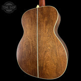 The back of an acoustic guitar made of rich brown wood with a light cream binding, shown against a solid black background. A Tone Shop watermark is visible in the top left corner.