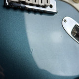 Close-up of a blue electric guitar with a pickguard and control knobs.