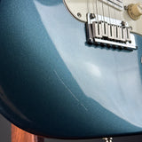 Close-up of a blue electric guitar with a focus on the neck and bridge.