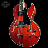 Red electric guitar with a black background, featuring the Tone Shop logo.