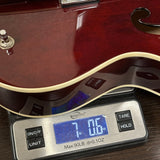Guitar being weighed on a digital scale with a wooden finish.